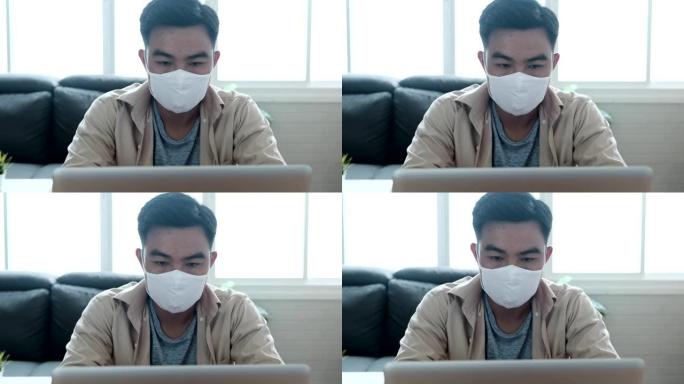 亚洲男子坐在办公桌前，打喷嚏护卫，在家庭办公室使用笔记本电脑，戴着防护口罩，在新型冠状病毒肺炎大流行