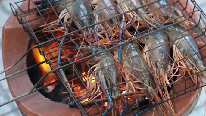泰国河虾在木炭烤架上烤，在烧烤泰国铁烤架上烤。在泰国街头美食夜市的炭炉上煮巨型烤龙虾。烤巨型河虾。