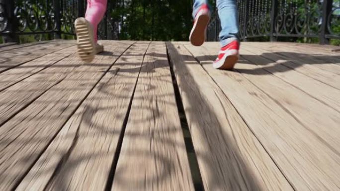 欢快的孩子们牵着手在桥上的公园里奔跑。慢动作镜头