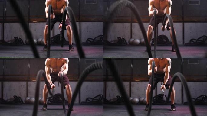 英俊的肌肉裸胸运动员与战斗绳索在健身馆锻炼。慢动作