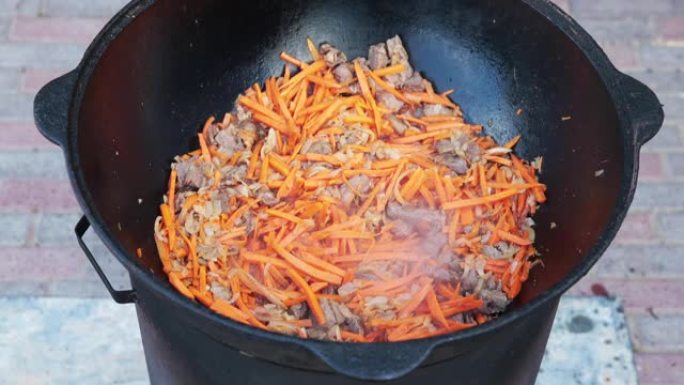 在大锅中准备乌兹别克斯坦国家菜抓饭，抓饭，plov，胡萝卜配肉。烹饪过程，开火。在火锅里做饭。用撇渣