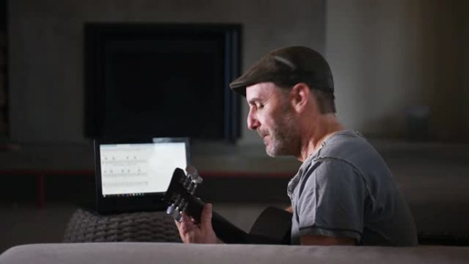 家庭独自吉他爱好成熟的男人用笔记本电脑练习吉他