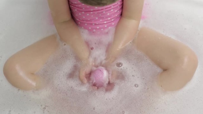 女孩的手把洗澡炸弹放在水里。浴盐球溶解在水中