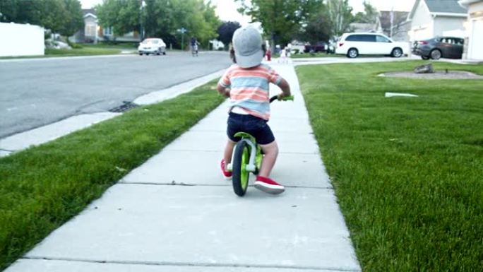两岁男孩在中产阶级社区骑自行车，祖母看着他