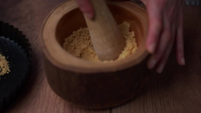 用带有杵的木制研钵中的饼干制成的细碎粉末状dame倒在专业的不粘蛋糕盘中。