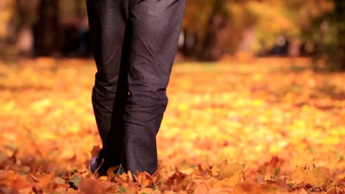 男人在秋天的公园里带着黄树散步。脚从相机上移开。