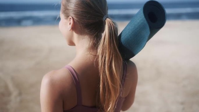背面视图，穿着运动服和体操垫的年轻女子去海滩