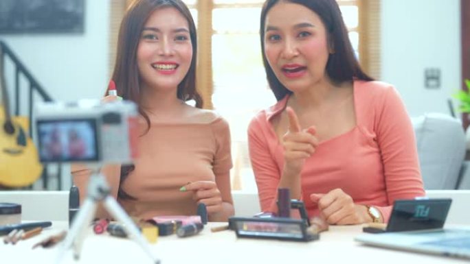 快乐微笑的两个年轻的亚洲女人或美容博主在录制视频和挥手的同时交谈和看着相机，在家工作的概念。美女视频