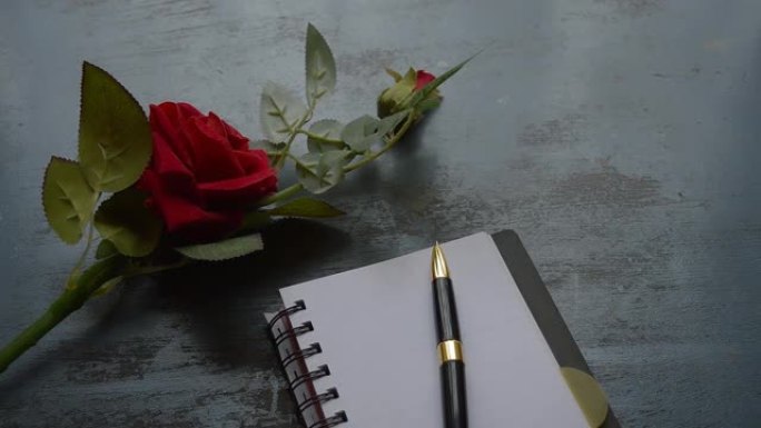 空白页笔记本、钢笔和乡村金属地板背景上的美丽红玫瑰，带有复制空间。情人节婚礼和假期的情书写作建议或建