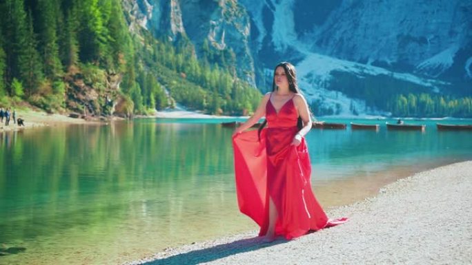 神秘性感的女人走过奢华的红裙。幻想迷人的设计长发丝绸飘飘。慢镜头自然，令人惊叹的风景布雷斯湖，白云石