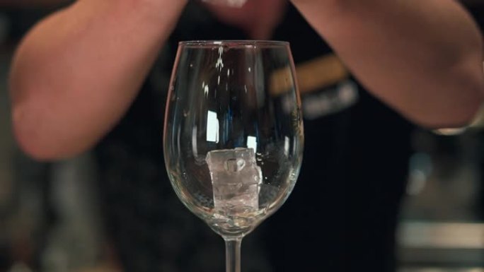 一个人把冰块扔进玻璃杯里。在夜总会或酒吧，专业调酒师准备加冰鸡尾酒