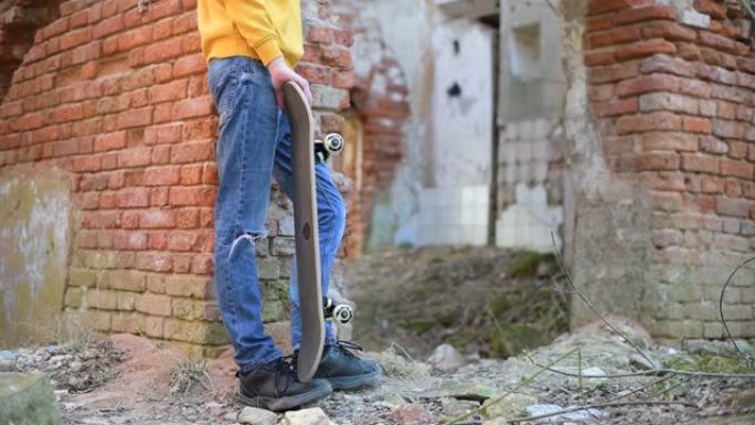 一名少年用滑板站在一座破旧建筑的墙壁附近