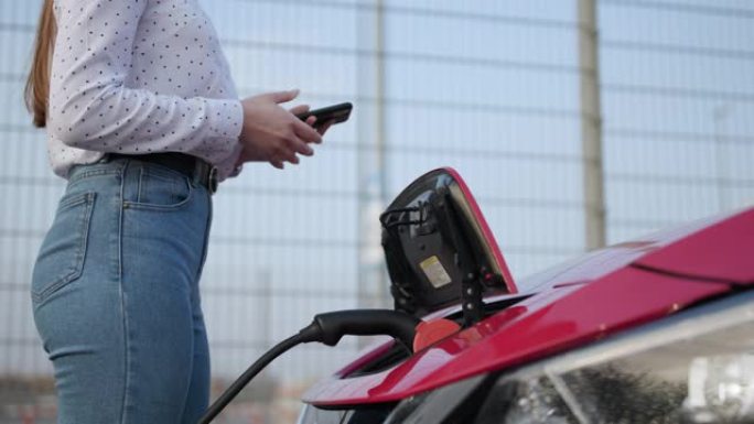 女人让电源插入正在充电的电动汽车。女人将充电器插入她的现代新型电动汽车的插座