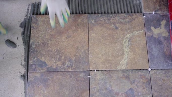 在地板上铺设瓷砖，主人将瓷砖放在用梳子涂的瓷砖胶水上