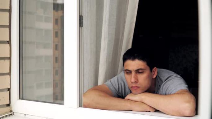 一个悲伤的家伙站在窗前。隔离和检疫期间的抑郁和问题。