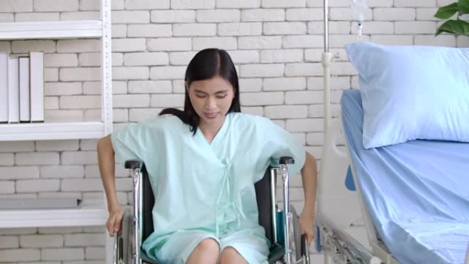 在医疗中心或医院的窗户旁边，病人床的房间里坐着并向前移动轮椅的亚洲病人妇女。接到通知后，她高兴地笑了