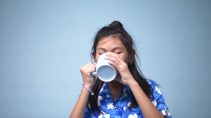 亚洲女孩喝蓝色杯子和蓝色背景。