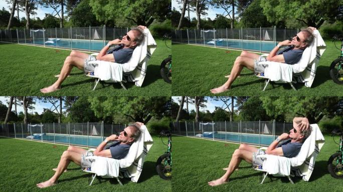老人在带游泳池的室外后院家庭花园休息。白天戴墨镜的老年人
