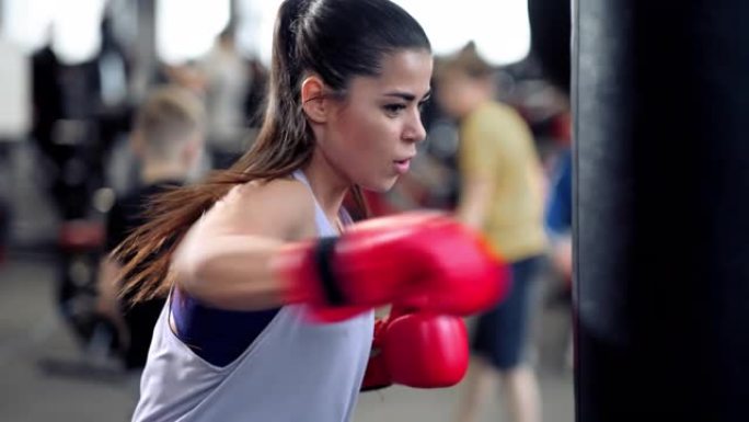 运动年轻的黑发女人在运动服装和红色拳击手套训练撞在一个拳击袋在健身馆。