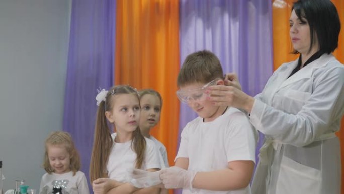 儿童化学实验。儿童有趣的实验。一名妇女进行认知科学课程。男孩戴着安全眼镜，戴着透明手套。