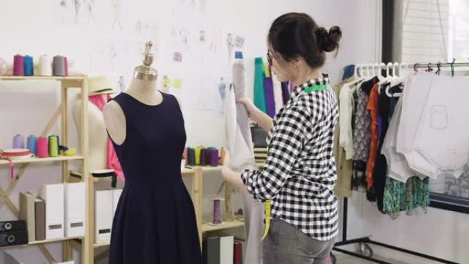 慢动作亚洲时装设计师在家庭办公室工作，测量人体模型面料。创意工作室的年轻女孩裁缝设计新的季节系列比较