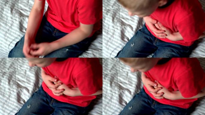 小男孩把手放在肚子上，痛苦地扭动着。腹痛一个孩子。