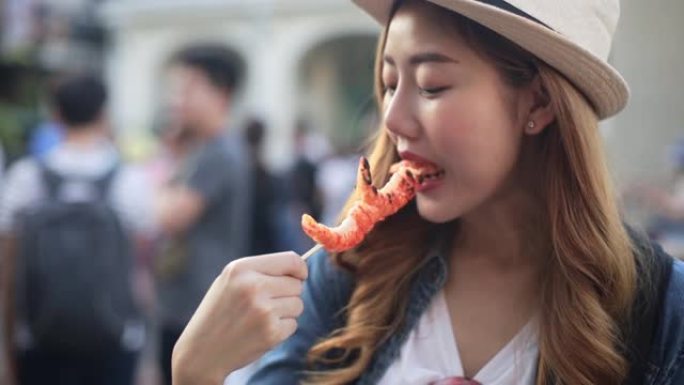 亚洲年轻女子在曼谷市市场吃传统的亚洲街头食品。美女吃泰国街头食品的特写。