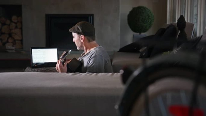 家庭独自吉他爱好成熟的男人用笔记本电脑练习吉他