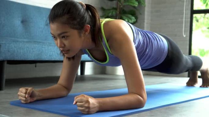 20多岁的年轻亚洲女性穿着运动服，一边在电脑笔记本电脑上在线观看健身训练课，一边摆木板姿势。健康女孩
