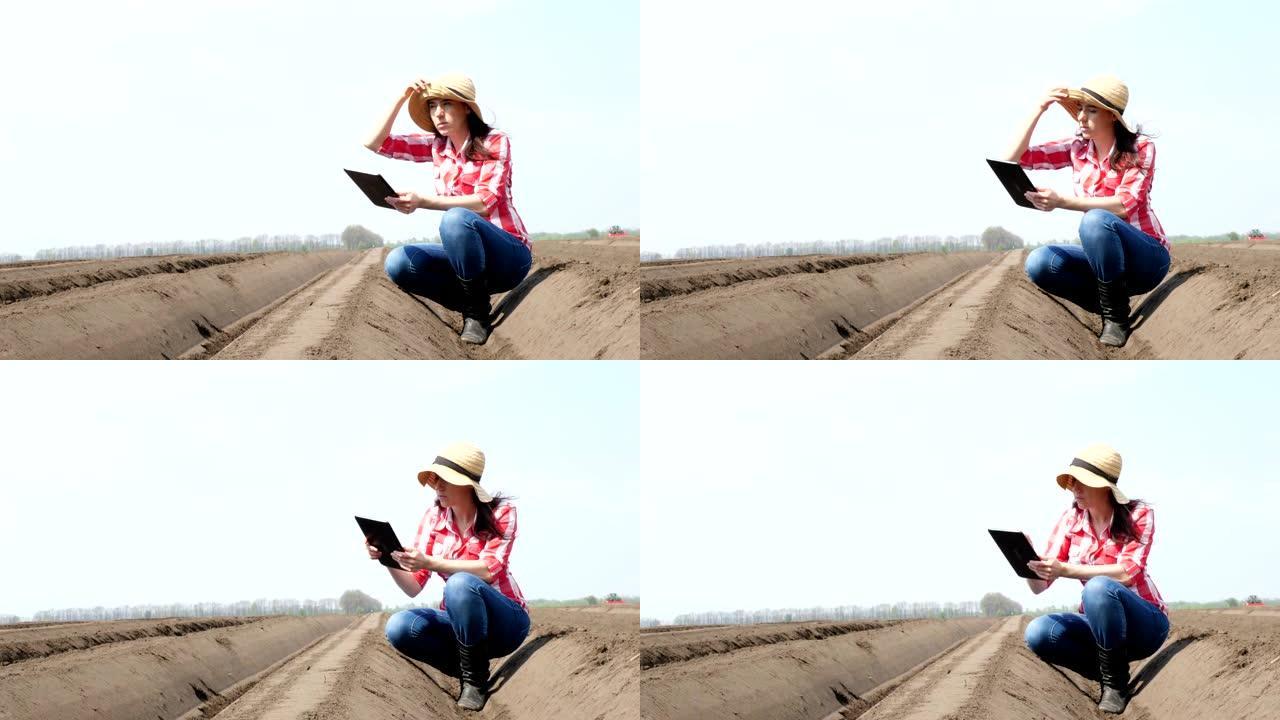 女农民，农艺师坐在田间特殊的土壤行之间。她使用片剂测试了中耕者种植马铃薯的质量。现代农业马铃薯种植。