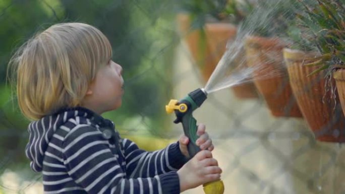 小男孩在花园的房子里玩软管和水