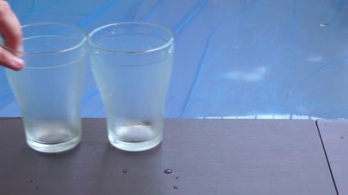 一只手在游泳池的侧面放了两个玻璃杯