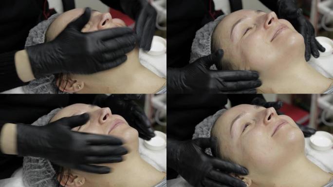 美容师在美容诊所沙龙的女性脸上涂抹保湿霜