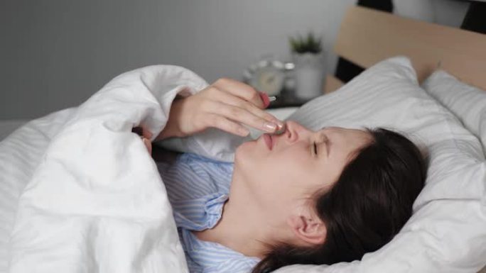 生病的女人流鼻涕躺在毯子下的床上，用移液器滴下的滴水滴鼻子。感冒，流感，过敏，鼻炎，体温过低，干燥空
