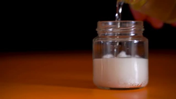 在加入醋的玻璃罐中放入小苏打。有趣的化学效应。黑暗背景下的视频概念