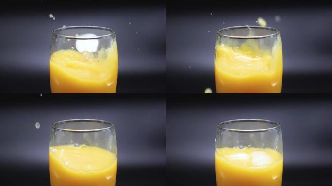 冰块落在黑色背景上的橙汁玻璃杯中。慢动作500 FPS