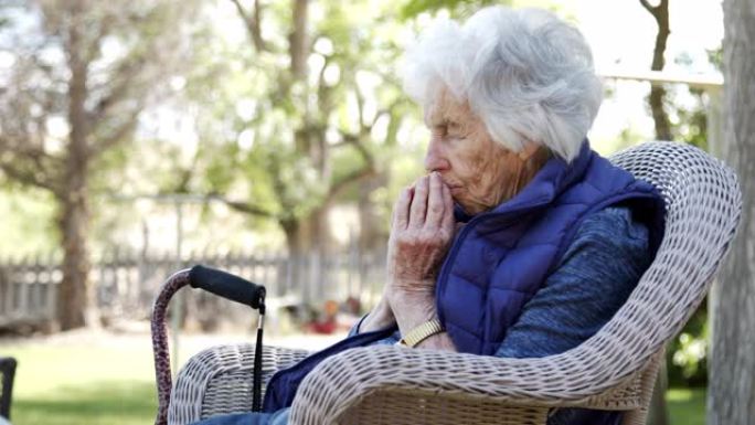 夏天，一名老年白人基督教高级妇女在户外的草坪椅上闭着眼睛祈祷的侧角轮廓照片