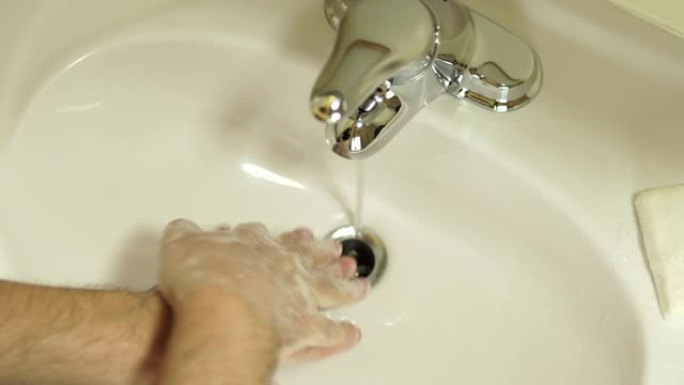 一个男人用肥皂砖和白色浴室水槽里的水洗手的特写镜头。健康福祉和身体护理概念。自我预防感染COVID 
