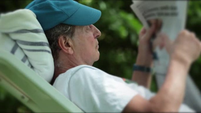 坦率的高级男子躺在外面放松，享受退休生活时阅读新闻