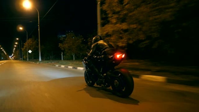 在小镇的夜间街道上骑着现代运动摩托车的人。摩托车手在夜城赛车。旅途中开车的人。自由和冒险的概念。后视