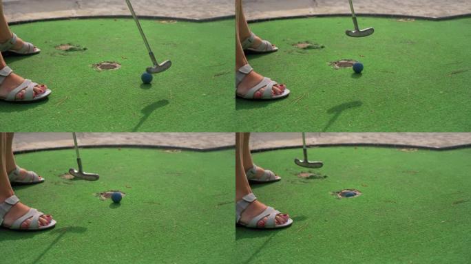 高级女子扮演迷你高尔夫球，在将蓝球放入洞中之前错过了轻松的投篮机会。绿色地毯上腿上的细节