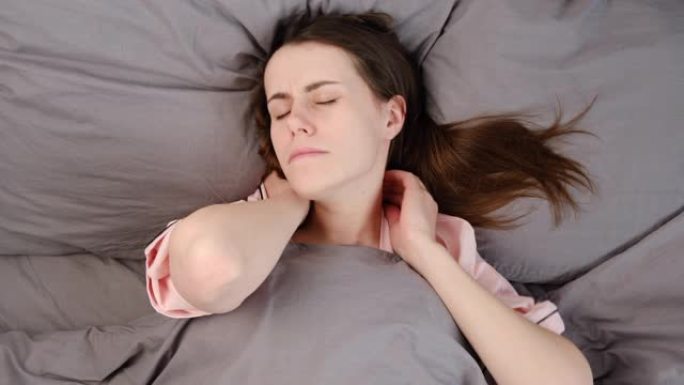 俯视图疲惫心烦的年轻女子按摩紧张的颈部肌肉躺在床上，缓解压力，疲惫的女孩痛苦不堪，感觉物理不适。纤维