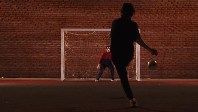 两个年轻的男人朋友晚上在操场上踢足球-一个人保护大门