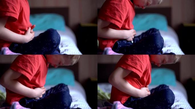 小男孩把手放在肚子上，痛苦地扭动着。腹痛一个孩子。