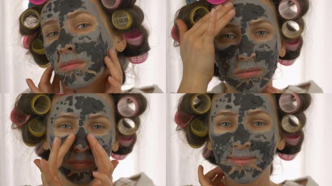 脸上戴着黑色粘土面具的女人看着相机，特写镜头。头上有卷发器的女性正在家里进行美容治疗。护肤和天然美容