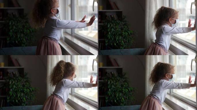 新型冠状病毒肺炎冠状病毒的概念，小女孩戴着面具透过窗户看，检疫在家里。检疫期间因COVID而悲伤的孩
