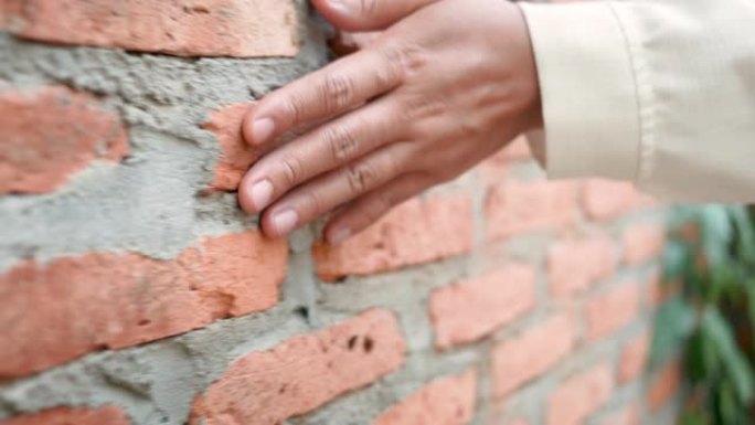 女人的手靠近用水泥墙触摸坚硬粗糙的砖面，是室外房屋墙壁的一部分。