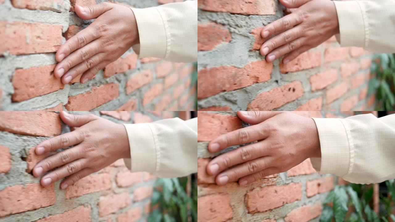 女人的手靠近用水泥墙触摸坚硬粗糙的砖面，是室外房屋墙壁的一部分。
