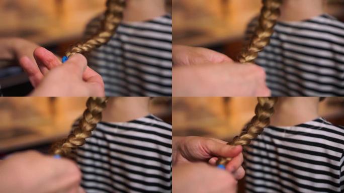 母亲的双手在厨房舒适的家中为女儿孩子长长的金发女孩穿着条纹连衣裙制作编织发型的辫子。妈妈在乎。母亲节