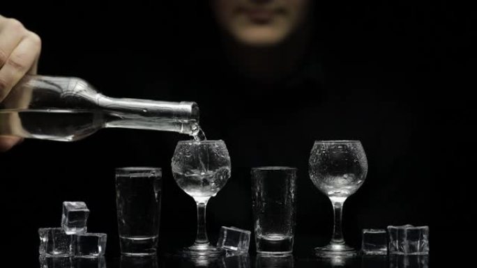 酒保将冷冻伏特加从瓶子里倒入加冰的玻璃杯中。黑色背景